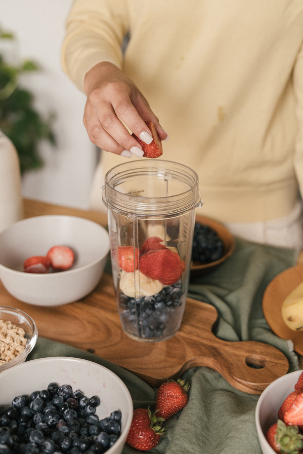 Person making energizing smoothie with bananas, strawberries, and blueberries