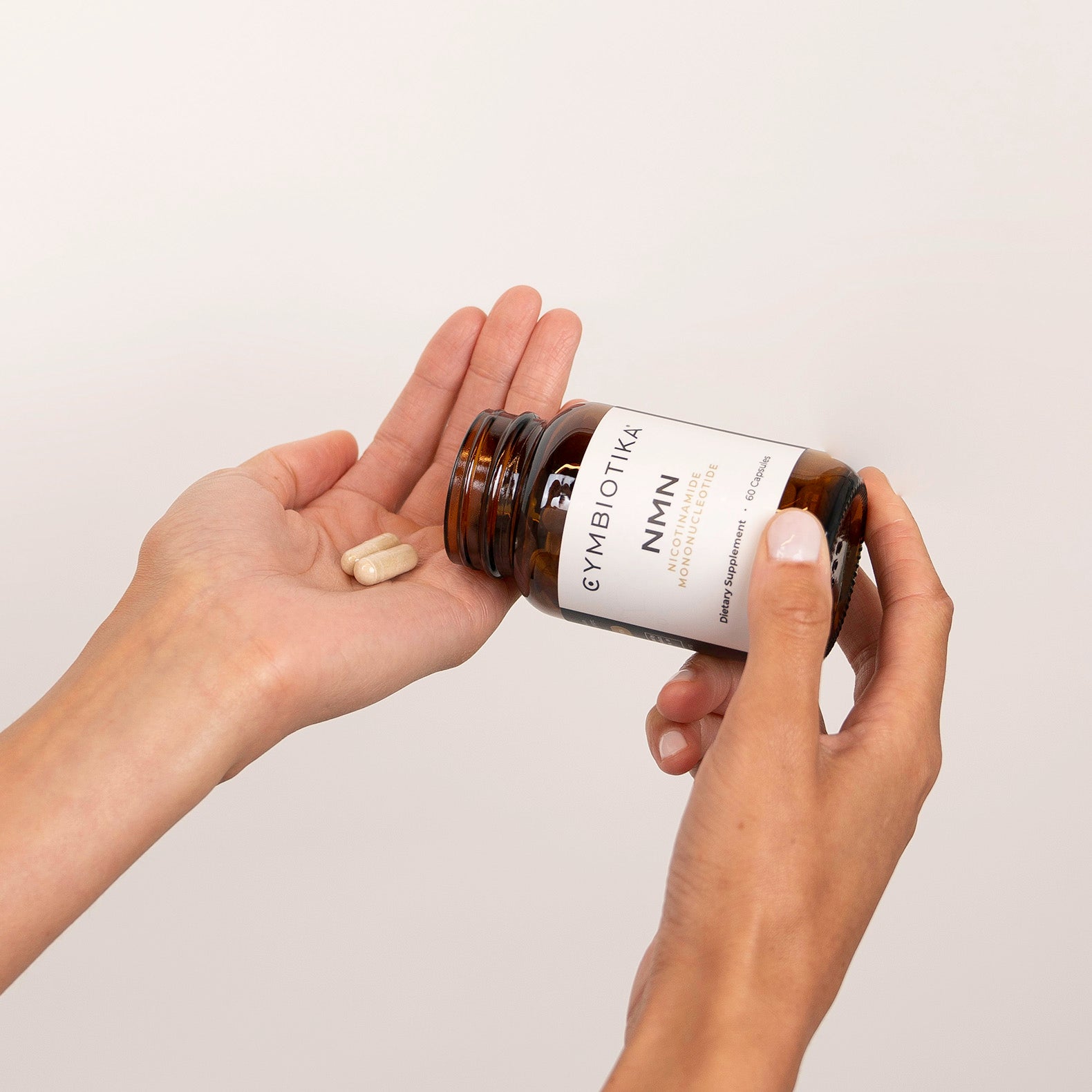 Woman emptying 2 NMN + Trans-Resveratrol capsules onto her palm